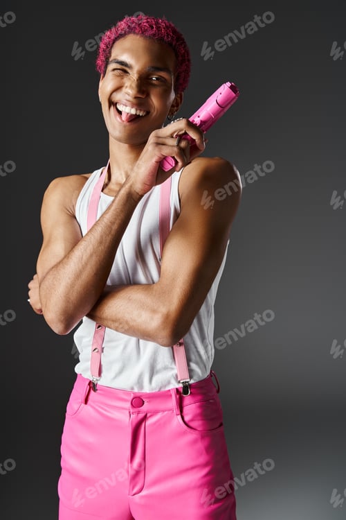 Preview: playful african american man sticking out his tongue and winking at camera with toy gun in hands