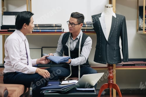 Preview: Tailor Shows Client Fabric Sample in Workshop