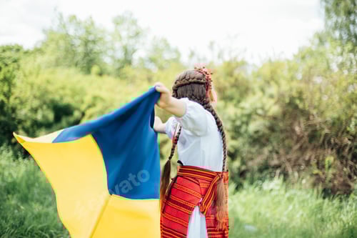 Preview: Ukrainian child girl in embroidered shirt vyshyvanka with yellow and blue flag of Ukraine in field.