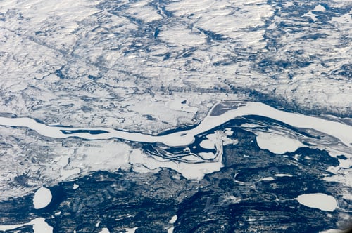 Preview: An aerial view of a snow-covered landscape with a winding river cutting through the icy terrain.