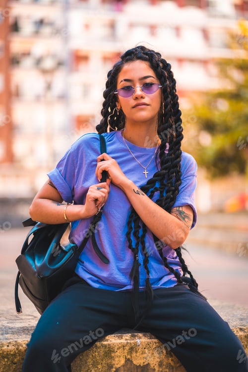 Preview: look of young dark-skinned woman with long braids and purple glasses sitting