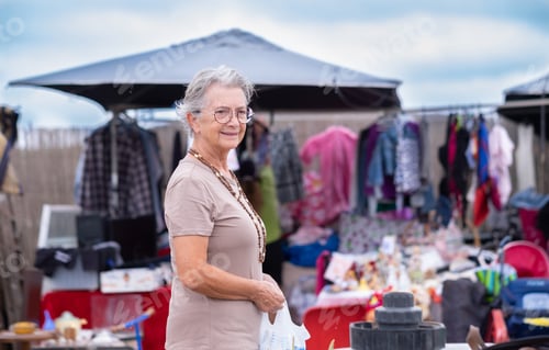 Preview: Senior woman at the flea market looking for second hand clothes, shoes, bags, jewellery