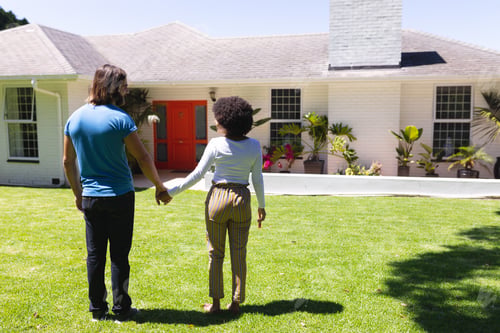 Preview: Happy diverse couple holding hands in front of house on sunny garden terrace