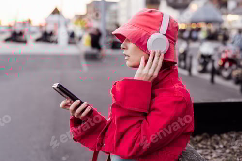 Preview: Stylish woman in viva magenta color jacket and bucket hat wearing headphones for listening music