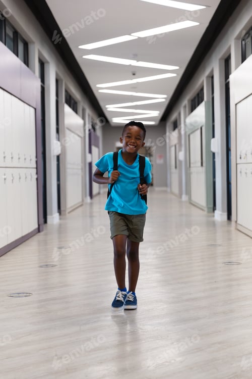 Preview: Portrait of smiling african american elementary schoolboy with backpack walking in school corridor
