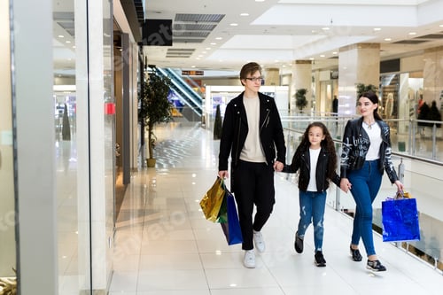 Preview: Happy young family with paper bags shopping at the Mall. Shop Windows with clothes