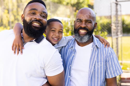 Preview: Hugging father and grandfather, smiling boy enjoying time with family outdoors