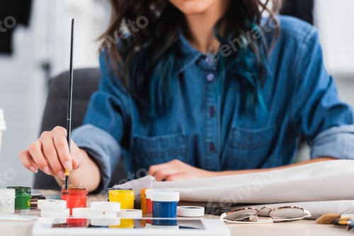 Preview: cropped image of female fashion designer painting on jacket at working table in clothing design