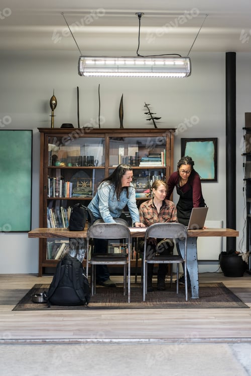 Preview: Three women gathered around table in office area of a metal workshop.