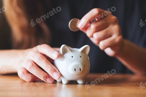 Preview: Closeup image of a woman putting coin into piggy bank for saving money concept