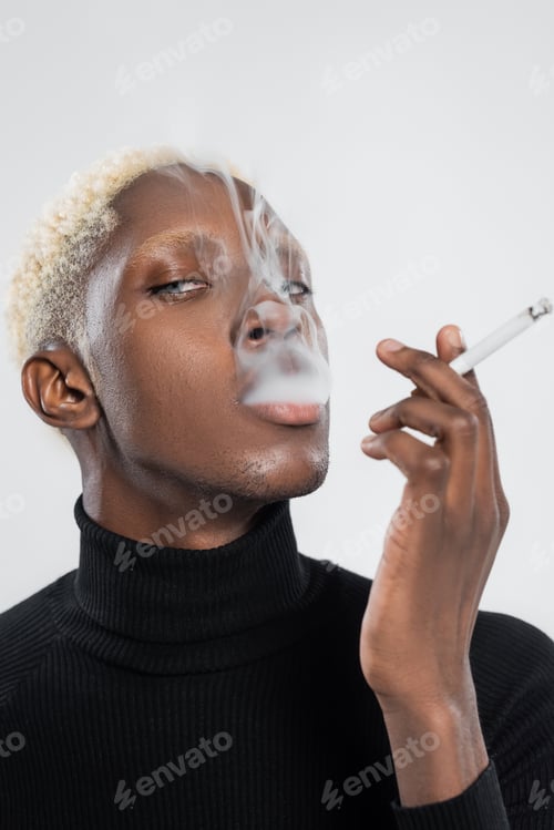 Preview: young and blonde african american man smoking cigarette isolated on grey
