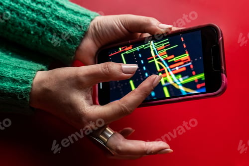Preview: Closeup of a female hand holding a phone with graphs on the screen on a red background
