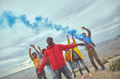 Preview: Playful Mood. Group Of Friends Standing On The Beach And Dancing While One Of Them Setting Blue