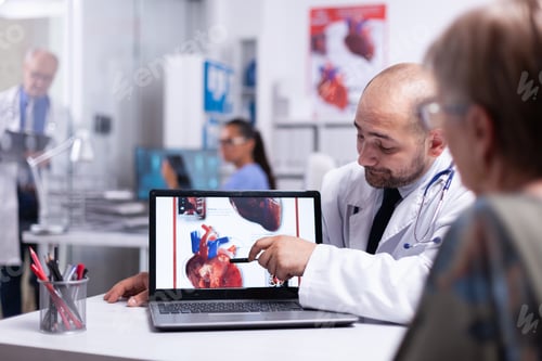 Preview: Physician using laptop showing heart disease to elderly woman
