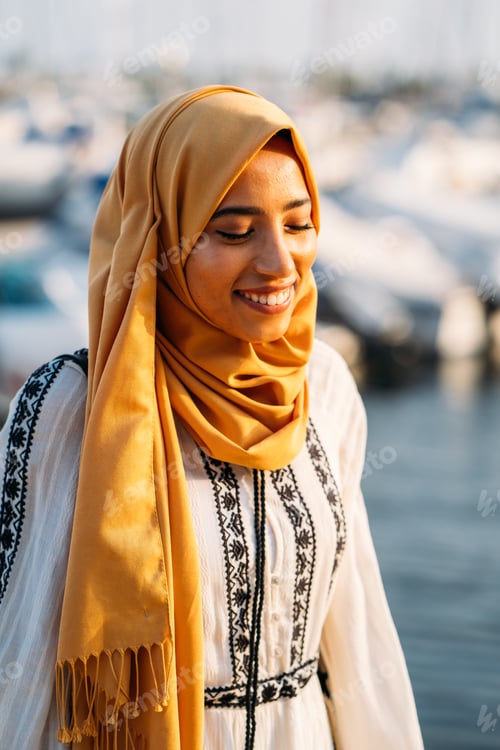 Preview: Young muslim woman smiling and wearing a yellow hijab in a marina