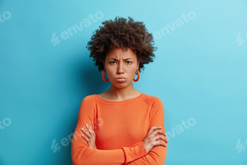 Preview: Horizontal shot of dark skinned offended woman with Afro hair keeps arms folded has offensive expres
