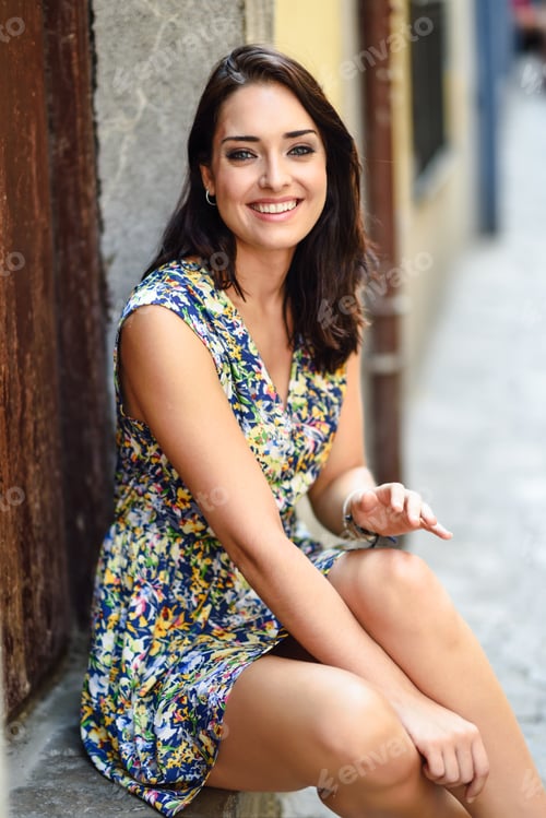 Preview: Happy young woman with blue eyes smiling sitting on urban step.