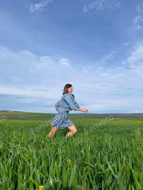 Preview: Lovely woman running through green grass field under blue sky