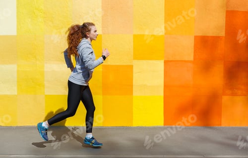 Preview: Side view of woman running against bright wall