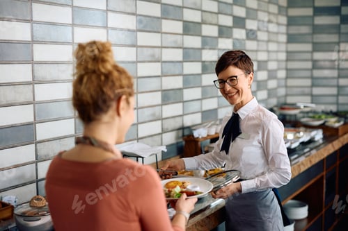 Preview: Happy waitress serving food to hotel guest during a breakfast.