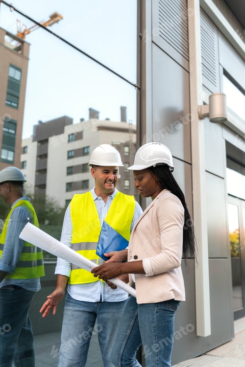 Preview: Two diverse Construction manager and architect reviewing blueprints on site outside office building