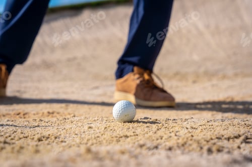 Preview: Detail the feet of a man playing golf, in the bunker hitting the ball with the pitching wedge stick