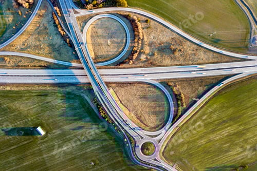 Preview: Aerial top view of modern highway road intersection, house roofs on spring green field background