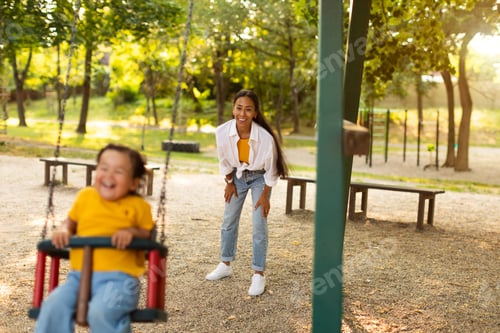 Preview: Joyful Asian Mother Swinging Toddler Daughter on Park Swing Outside