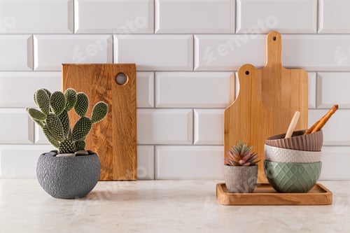 Preview: Set of ceramic bowls and cutting boards on stone light countertop in kitchen with potted opuntia