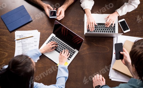 Preview: Overhead view of young businesspeople sitting together at workplace and using digital devices