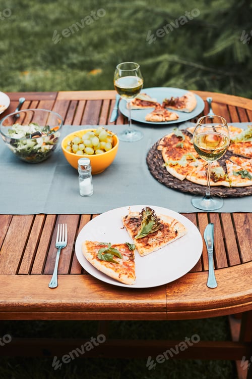 Preview: Dinner in a home garden. Pizza, salads, fruits and white wine on table in a orchard in a backyard