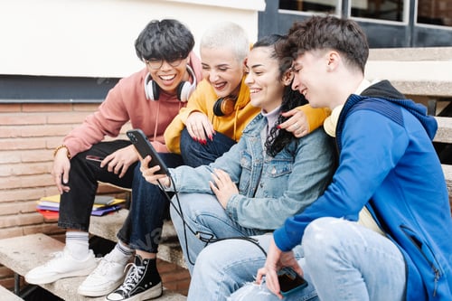 Preview: Teenager friends using cell phone. Students sitting in campus sharing funny video on the smartphones