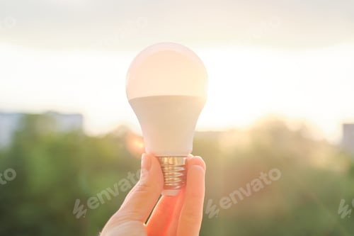 Preview: Led bulb, hand holding lamp, evening sunset sky background