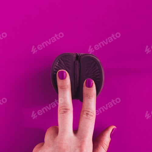 Preview: Vagina symbol. Two fingers on chocolate orange on purple background.