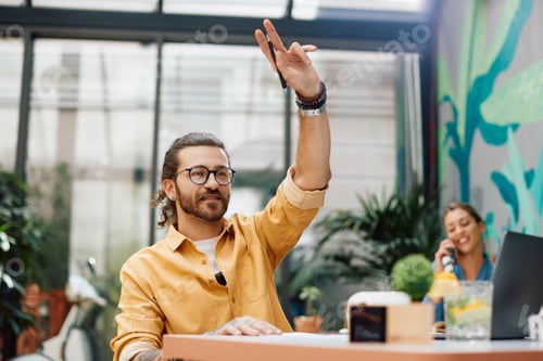 Preview: Young man with hand raised calling the waiter in a cafe.