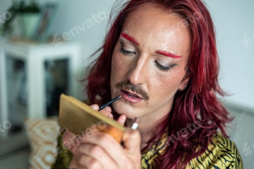 Preview: Young non-binary person applying lipstick at home
