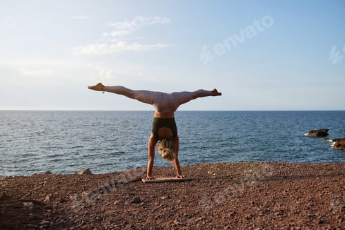 Preview: Woman doing the handstand yoga position in front of the sea