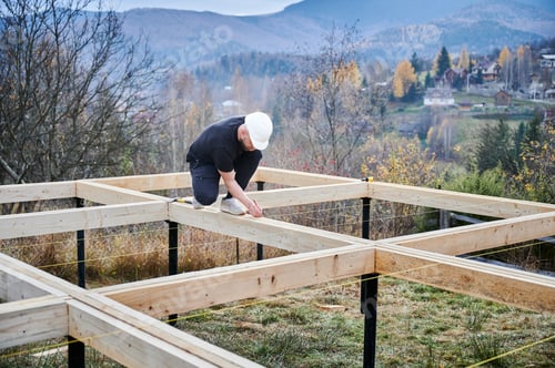 Preview: Man worker building wooden frame house on pile foundation.