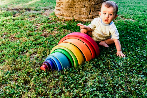 Preview: Baby girl playing with a waldorf material, a rainbow of wood montessori, in nature.