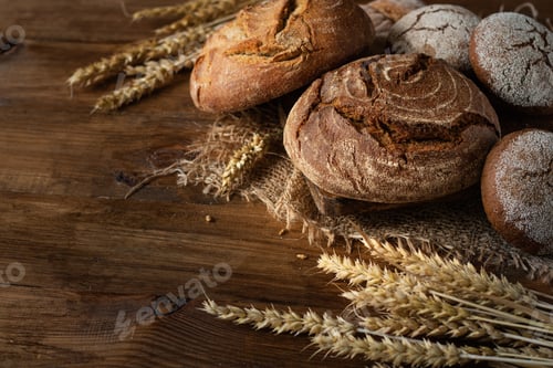 Preview: Freshly baked round bread and buns on burlap, on a wooden background. Next to the ears of wheat.