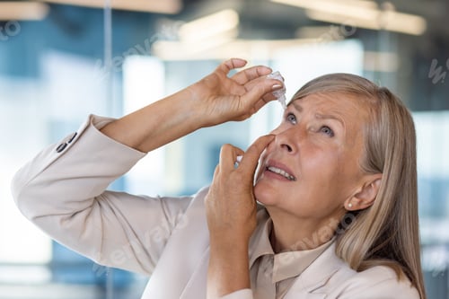 Preview: Scared business woman uses eye drops, gray-haired woman overtired sore eyes rubs medicine at