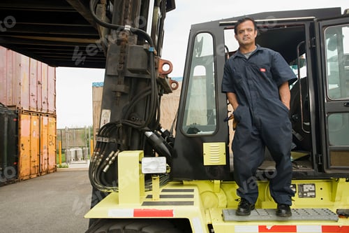 Preview: Confident worker posing with forklift at industrial site