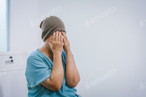 Preview: An elderly Asian woman wearing a gray-brown beanie, a light blue shirt, dark pants sits quietly