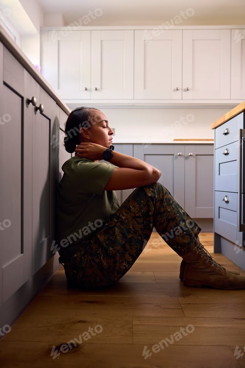 Preview: Depressed Female Soldier In Uniform Suffering With PTSD Sitting On Kitchen Floor On Home Leave