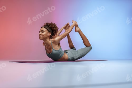 Preview: Sporty woman doing stretching exercises on yoga mat on studio background with color filter
