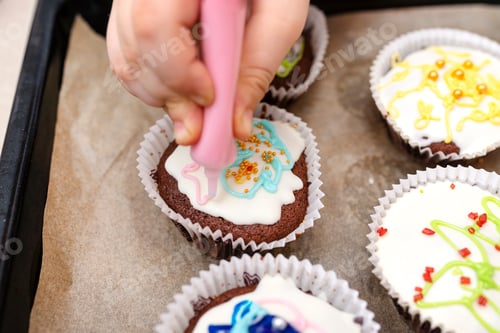 Preview: A child squeezes colored frosting from a tube onto chocolate brown cupcakes covered with white frost