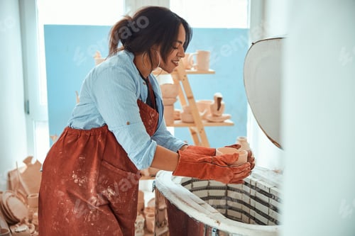 Preview: Charming female potter using electric pottery kiln in workshop
