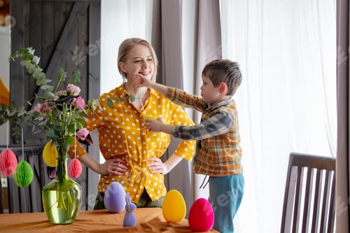 Preview: mother and son are decorating a table with paper eggs for Easter. Indoor