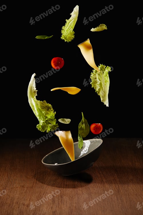 Preview: Fresh salad with cheese slices and bowl flying above wooden table surface