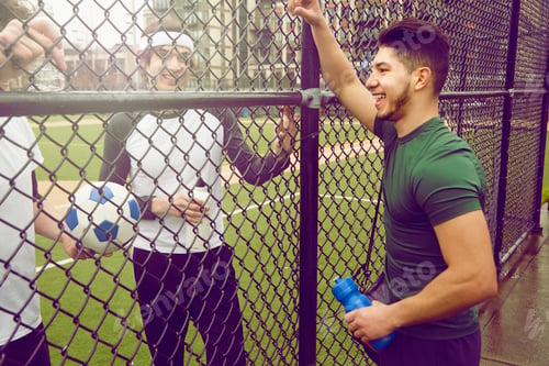 Preview: Three male soccer players chatting through wire fence